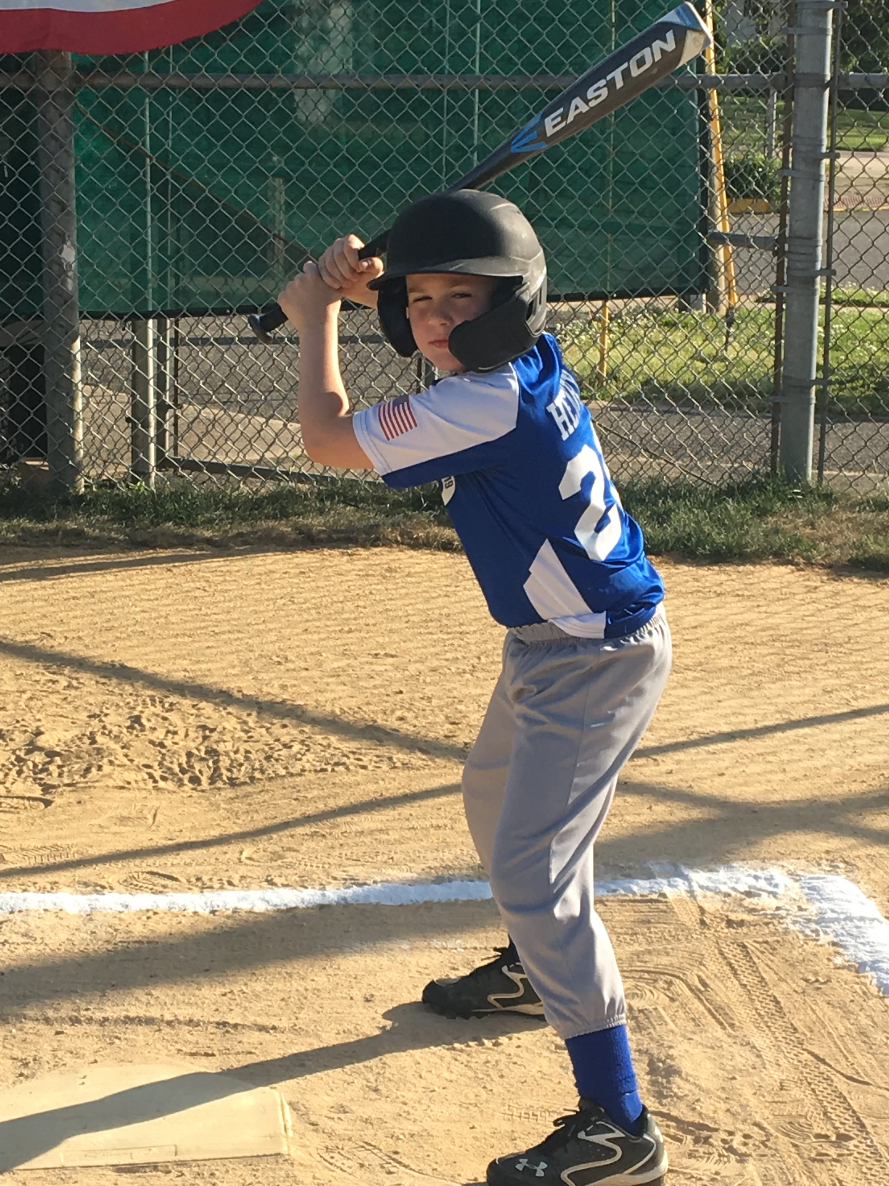 A young boy in a blue baseball uniform and batting helmet is posed at the plate, ready to swing a bat in a baseball game.