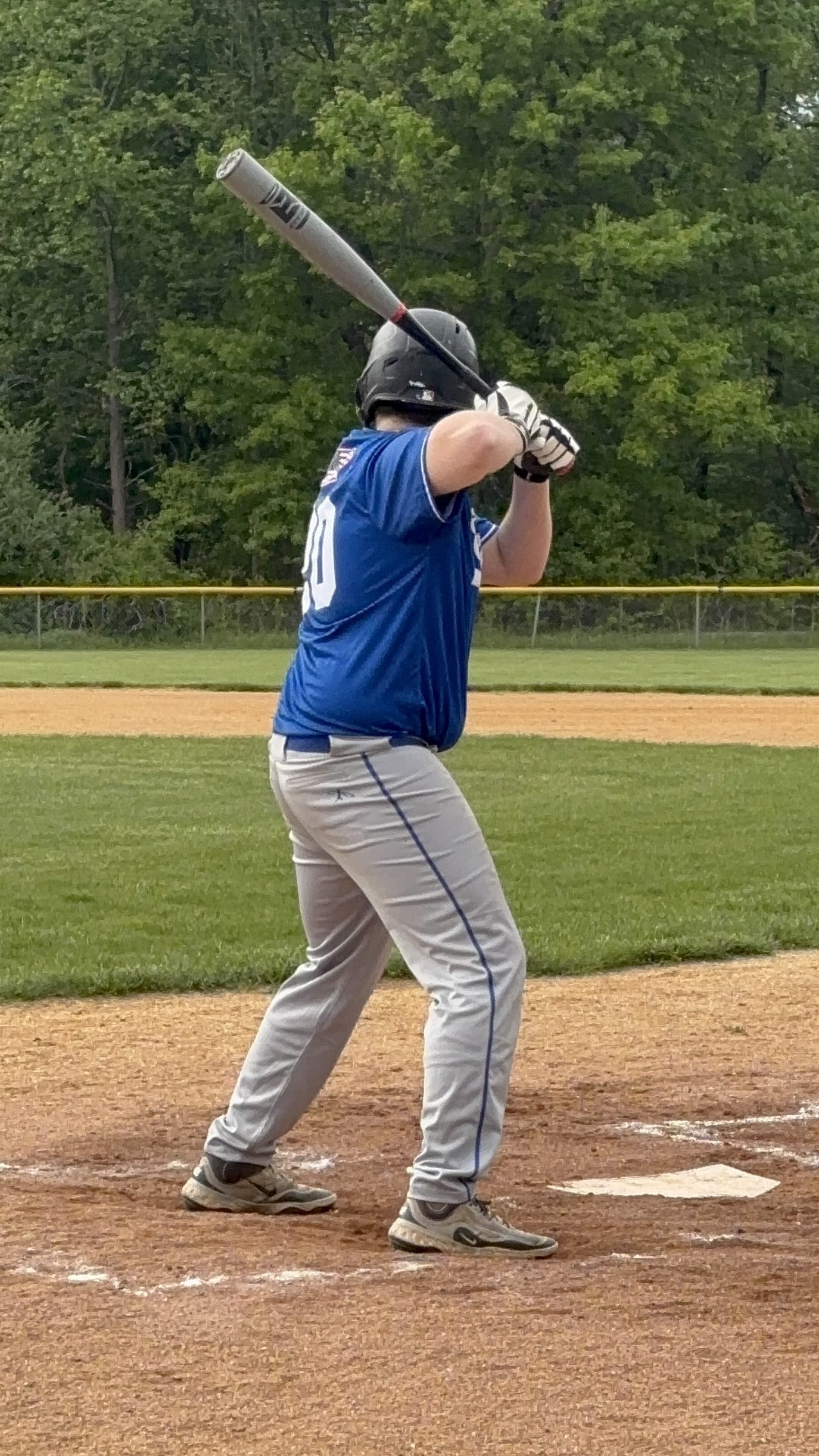 A baseball player in a blue jersey and gray pants stands in a batting stance on a baseball field, ready to swing a bat.
